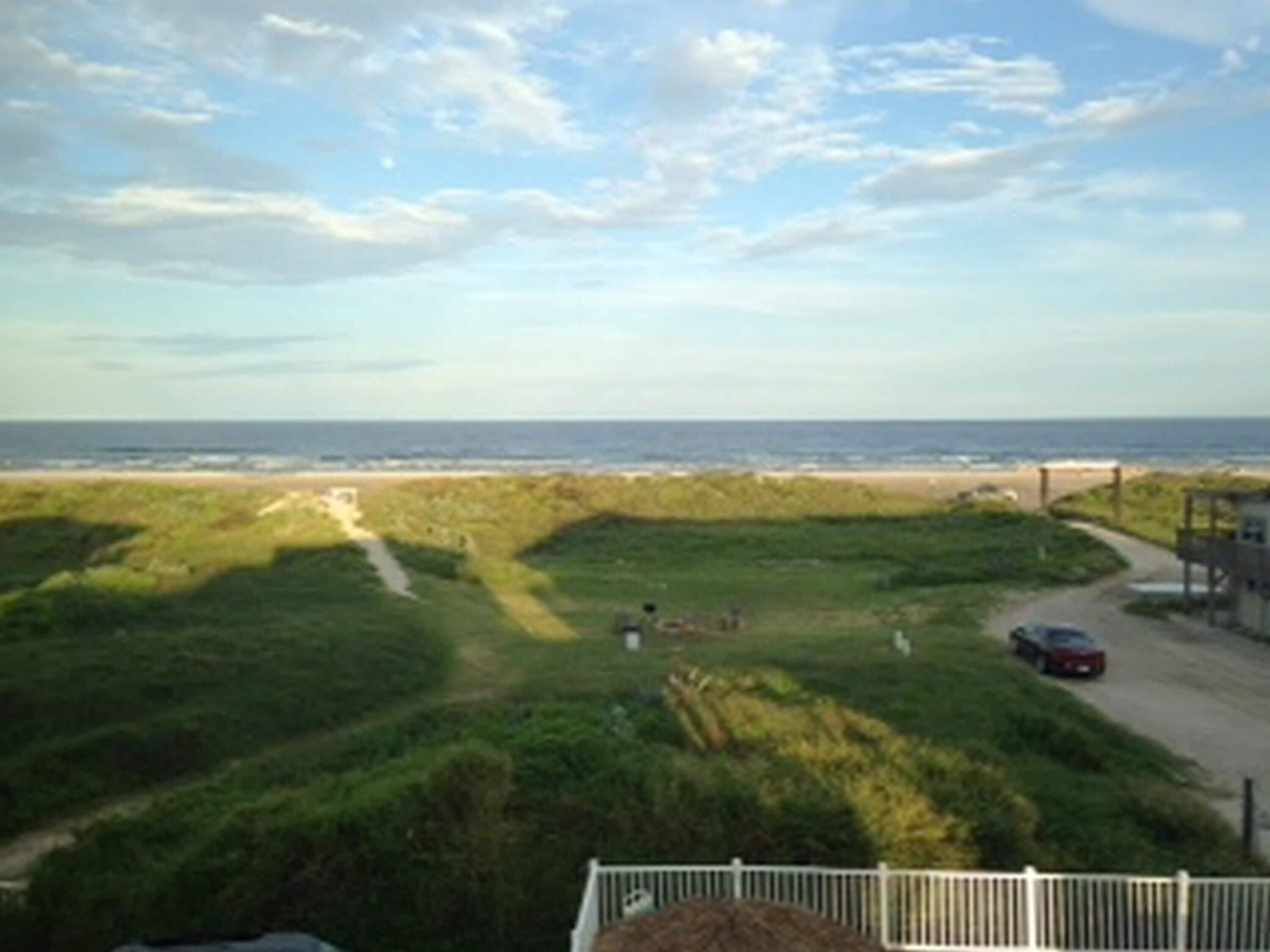 A coastal landscape with a beach, grassy dunes, and a road leading to a lifeguard tower.