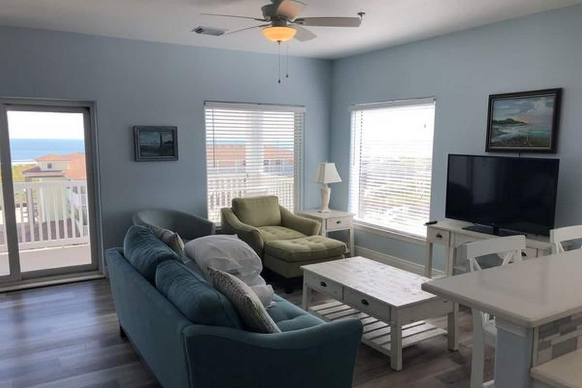 A living room with a sofa, armchair, coffee table, TV, and a ceiling fan.
