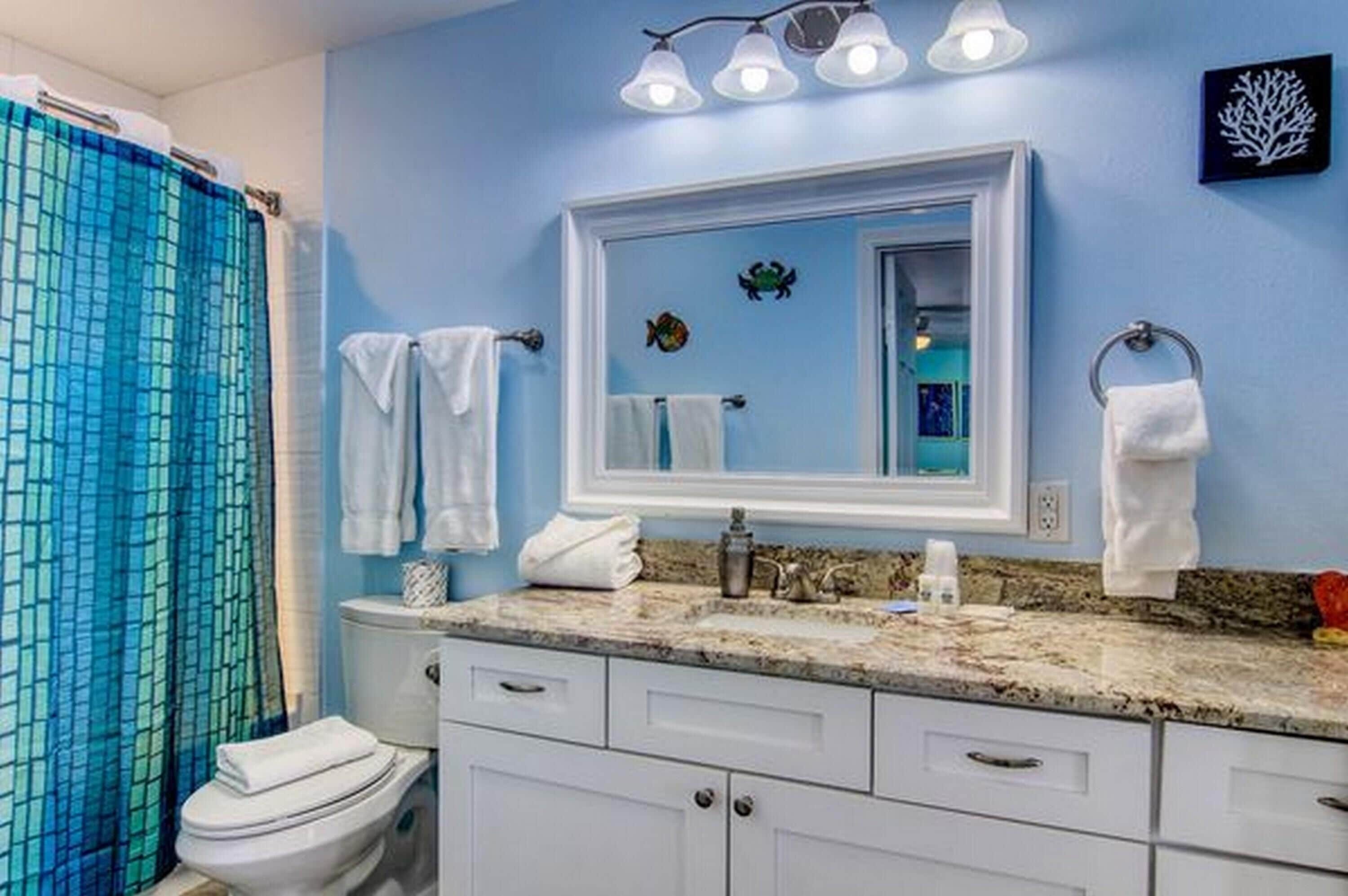 Une salle de bain avec un mur bleu, un lavabo blanc, un miroir et un rideau de douche.