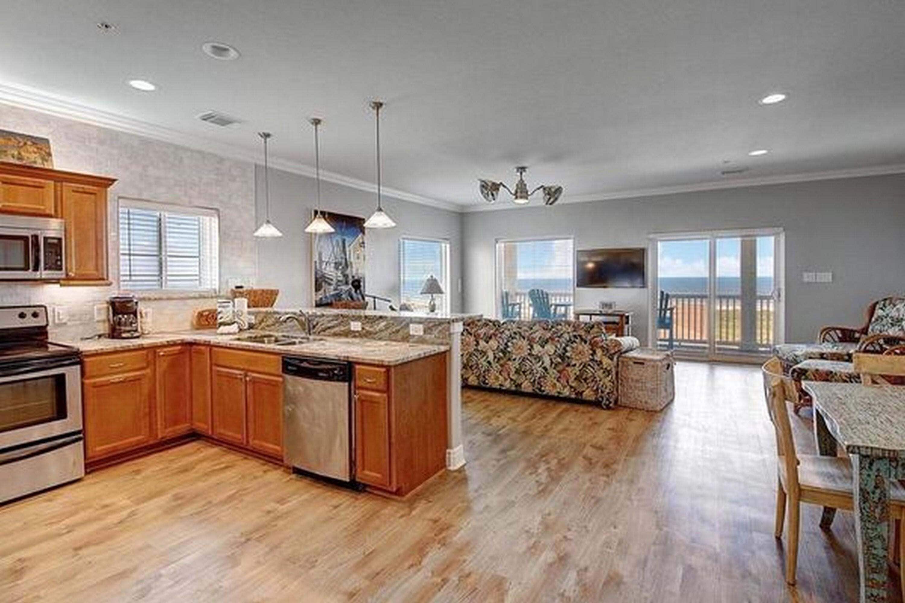A spacious kitchen with wooden cabinets, a built-in microwave, and a dishwasher. There is a dining area with a table and chairs, and a large window offering a view of the outdoors.