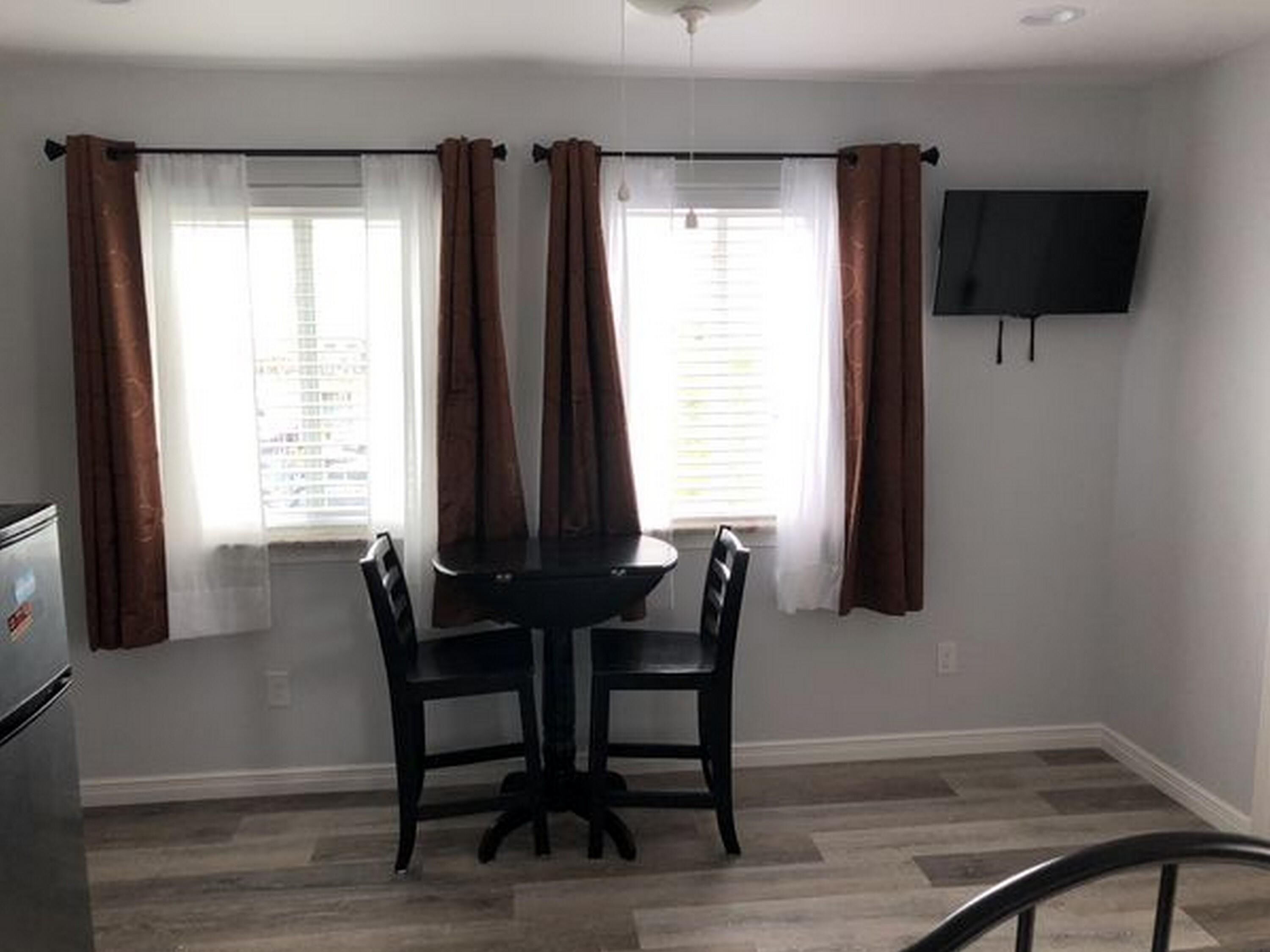 Un comedor con una mesa y sillas, un televisor en la pared y ventanas con cortinas.