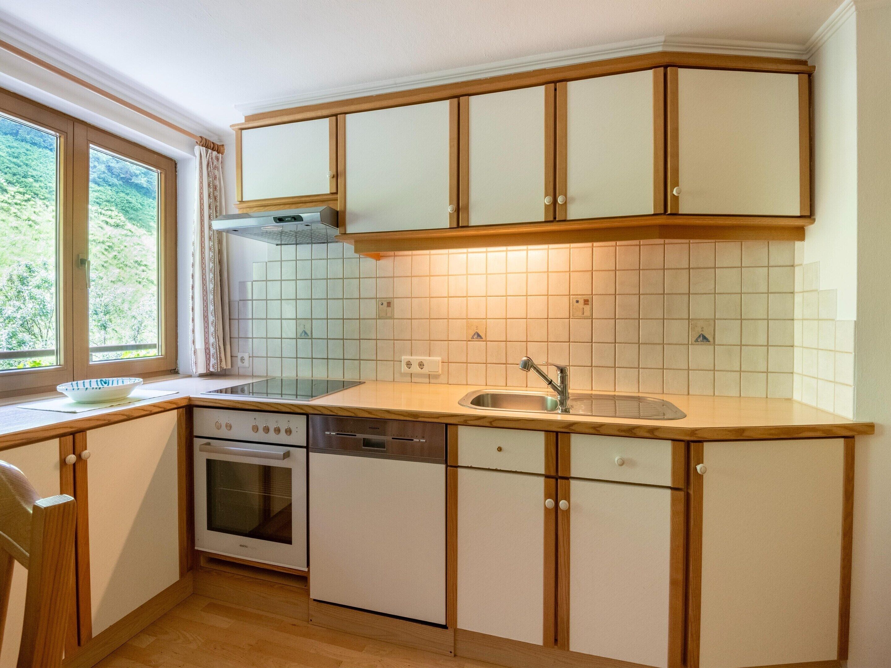 A compact kitchen with wooden cabinets, a built-in oven, and a window with a view of greenery.