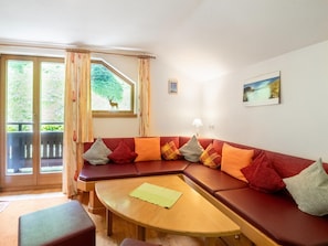 Una sala de estar acogedora con un sofá modular, una mesa de centro redonda de madera y un balcón con vistas a la vegetación y un ciervo.