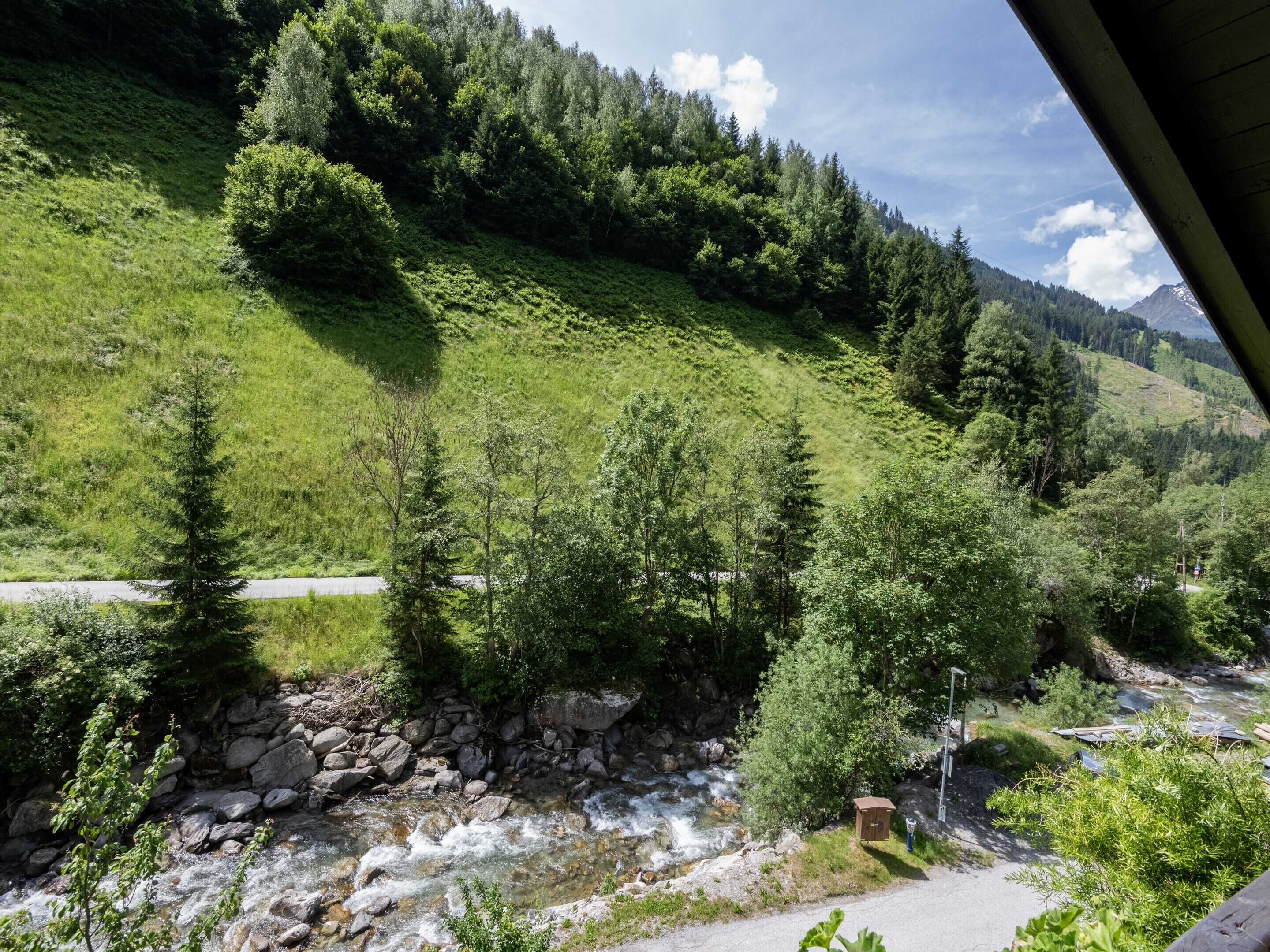 A mountainous landscape with a river, trees, and a small structure.