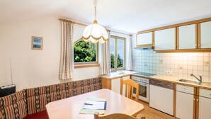 A compact kitchen with a dining area, a window with curtains, and a ceiling light fixture. - Chalet in Tirol by Zillertal Ski Slopes (Brandberg)
