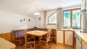 A compact kitchen with a dining area, wooden furniture, and a window with curtains. - Chalet in Tirol by Zillertal Ski Slopes (Brandberg)