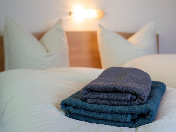 Una cama bien hecha con una toalla doblada, almohadas y una mesita de noche con lámpara.