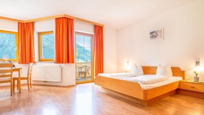 A hotel room with a wooden bed, a desk with a chair, and a view of the mountains through the windows. - Apartment in Neustift Near Ski Lift (Neustift Im Stubaital)