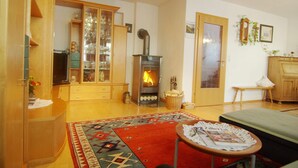 Ein gemütliches Wohnzimmer mit Kamin, einer Holzkabine mit Glastüren, einem gemusterten Teppich und einem kleinen Tisch mit Zeitschriften.