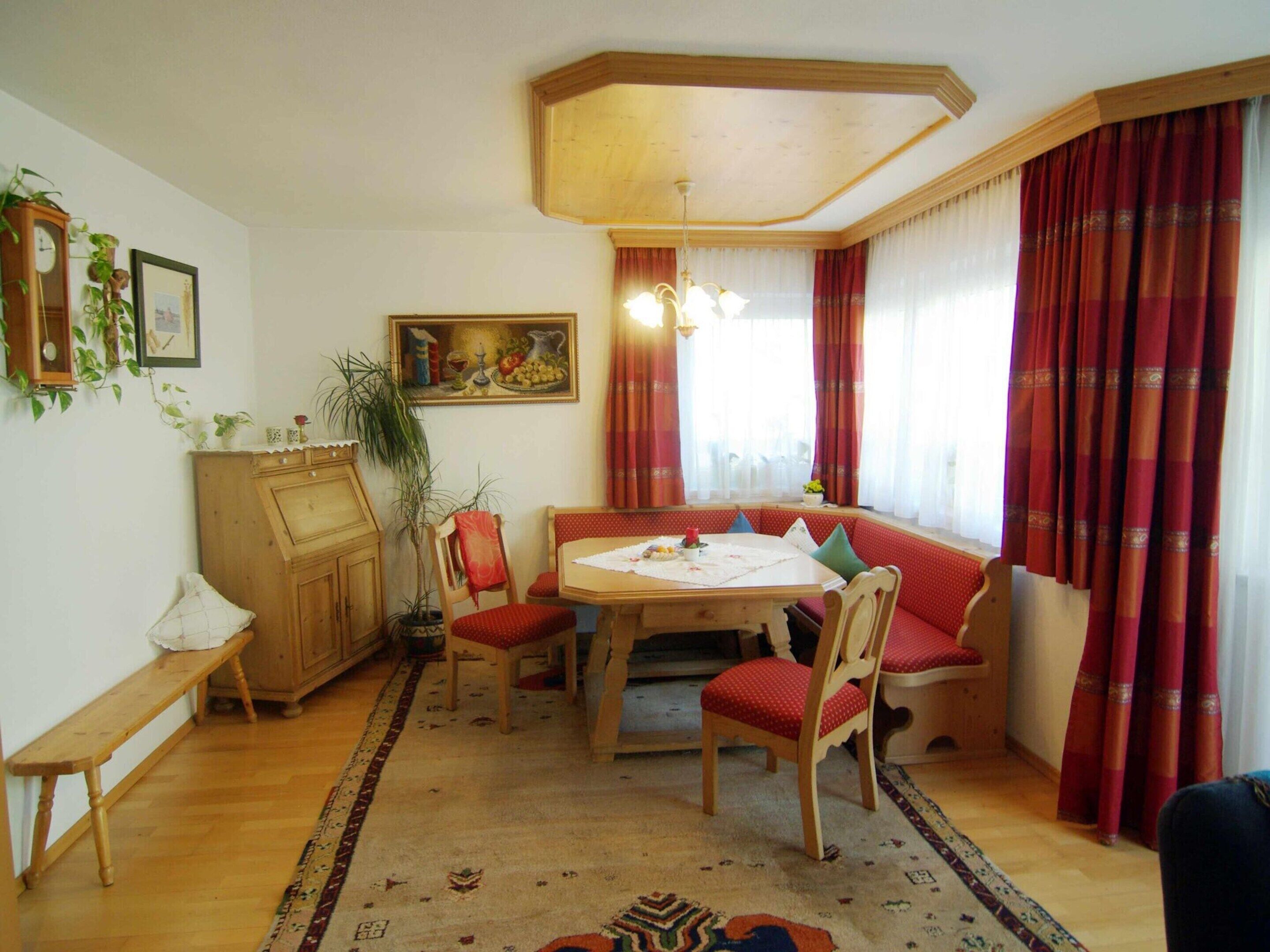 Een eetruimte met een houten tafel, rode bekleden stoelen, een bank en een schilderij aan de muur.