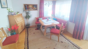 Ein gemütliches Wohnzimmer mit einem Holztisch, rot gepolsterten Sesseln, einer Bank und einer Topfpflanze.