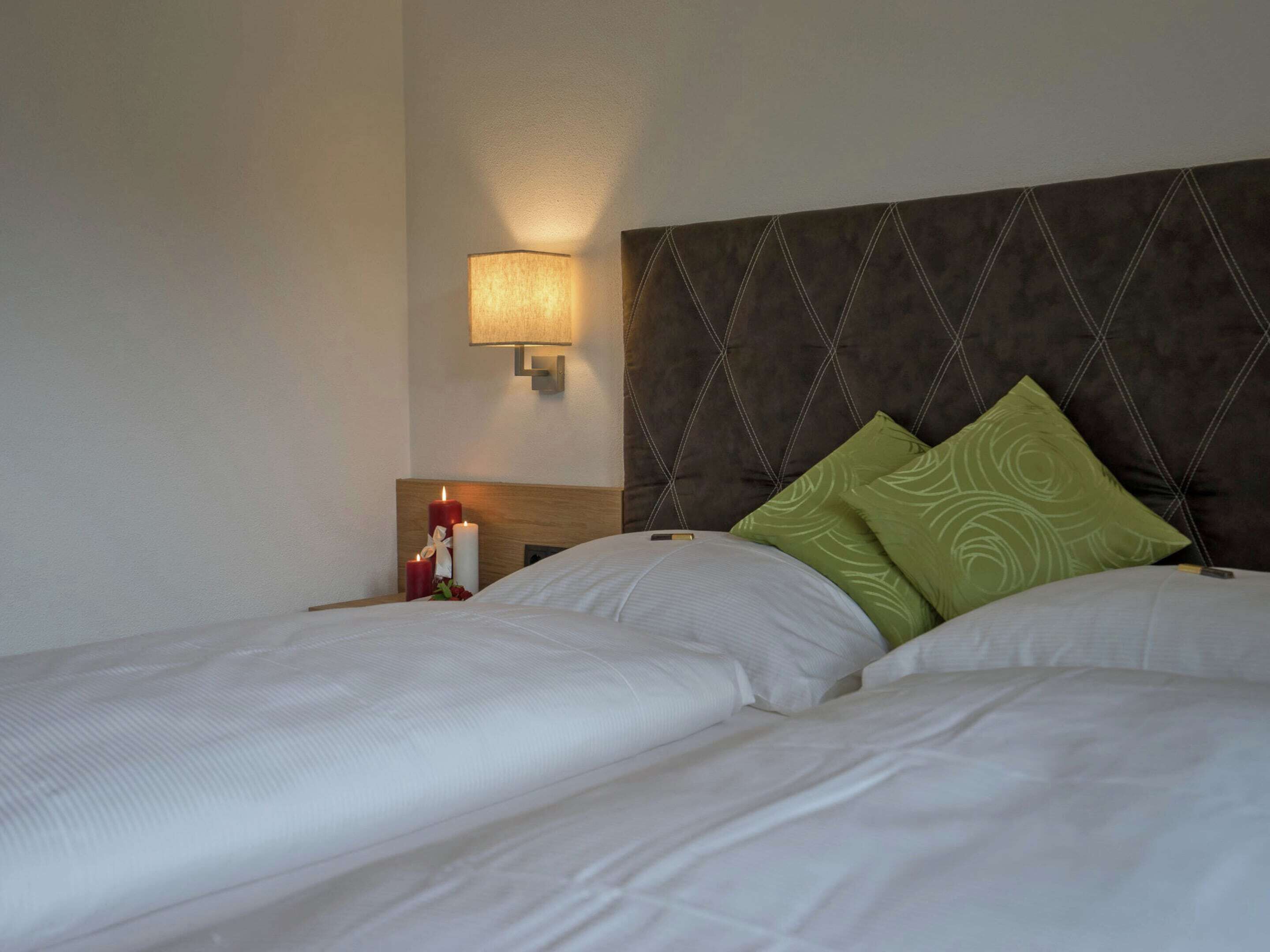 A hotel room with two beds, a nightstand, a wall-mounted lamp, and decorative candles.