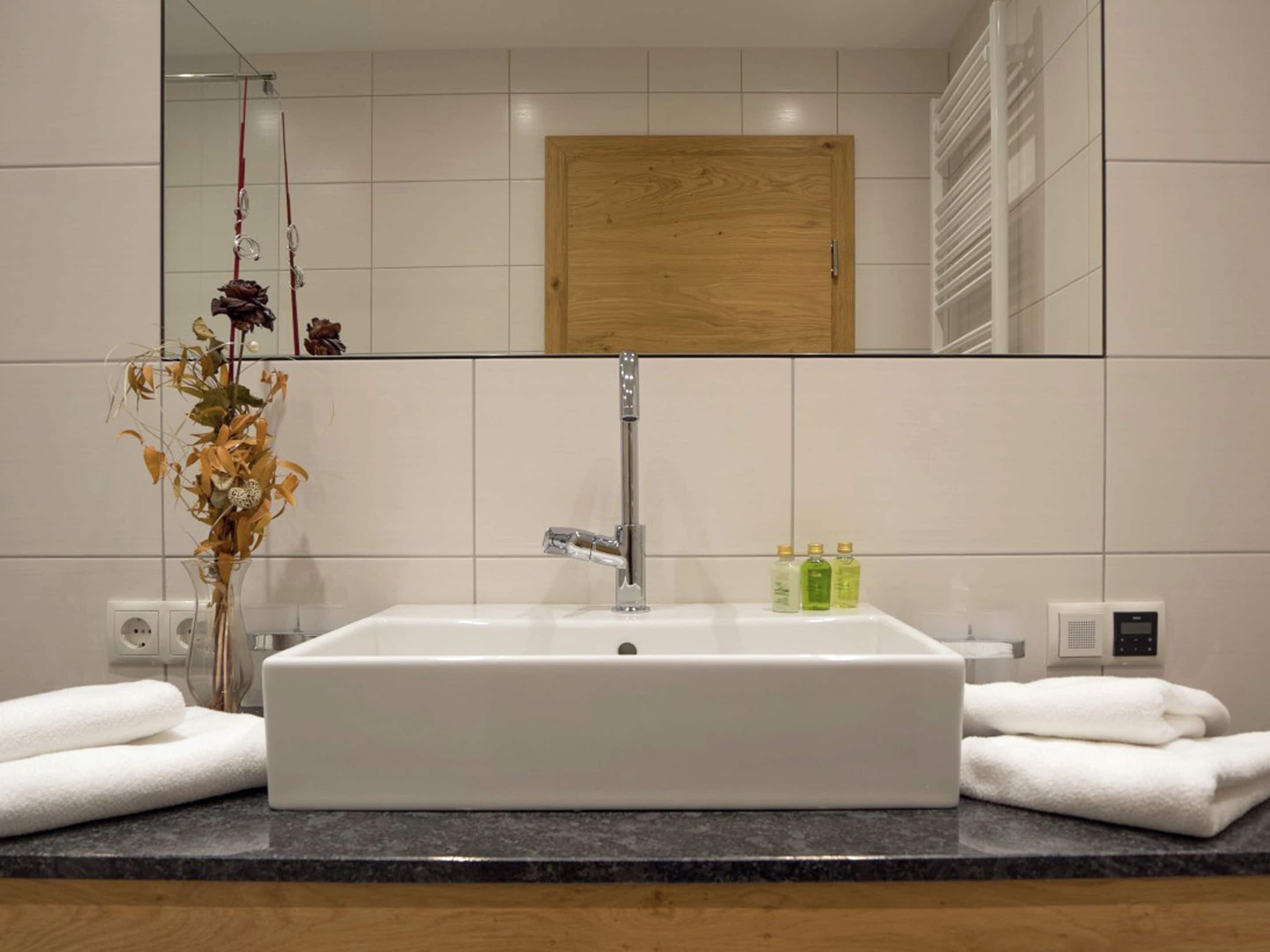 A bathroom with a white sink, a mirror, and a wooden cabinet above the mirror. There are towels on the counter and a vase with dried flowers.