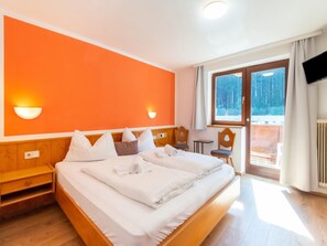Camera d'albergo con un letto grande, una testiera in legno, due comodini, un tavolino e una TV.
