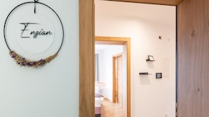 Ein Flur mit einer Holztürrahmung, einer Wanddekoration mit dem Namen 'Enzian' und einem Blick in einen Raum mit Bett und Nachttisch.