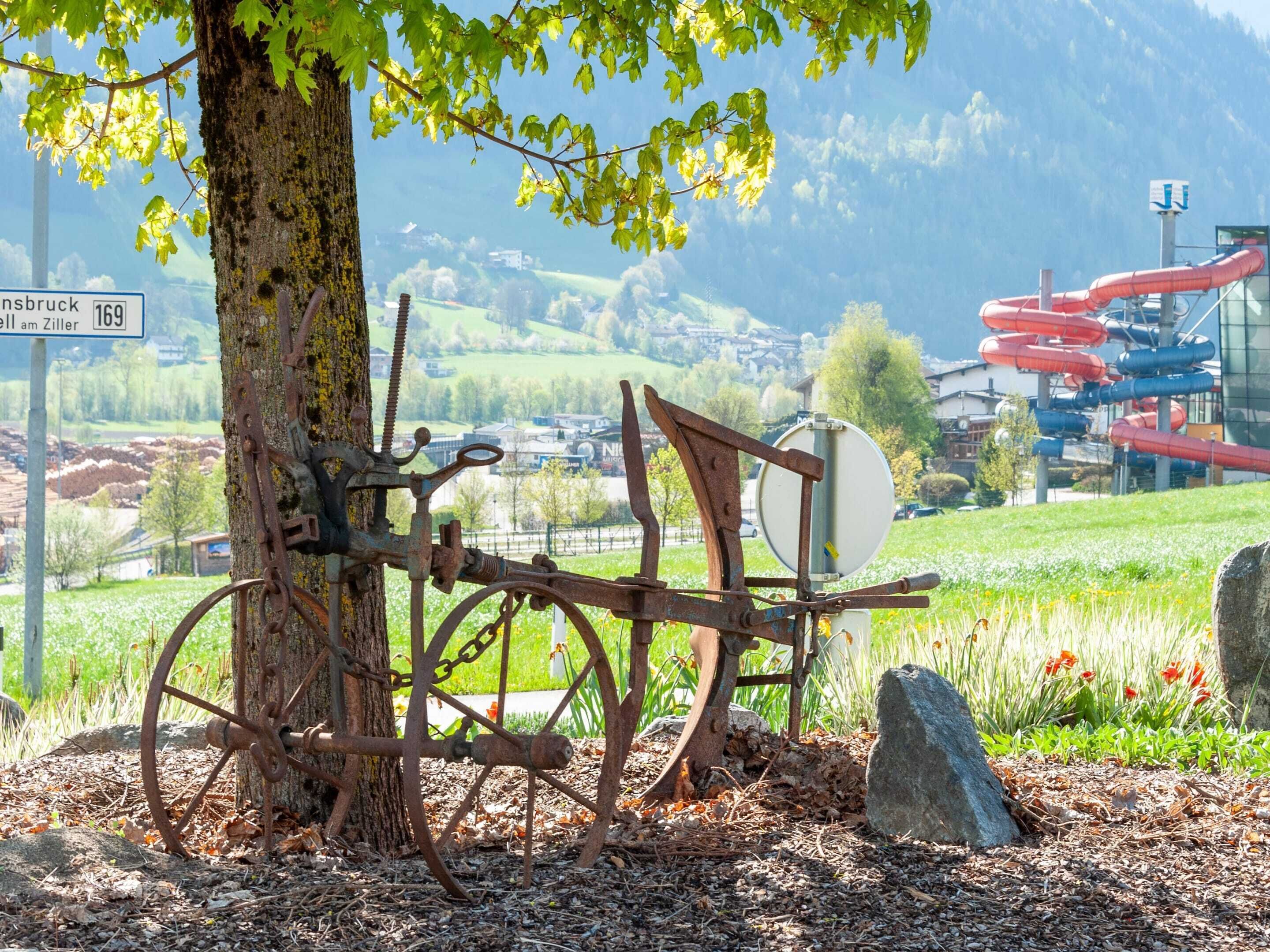 Une structure métallique rustique, agrémentée d’un arbre, se dressant sur un paysage pittoresque composé d’un village et de montagnes.