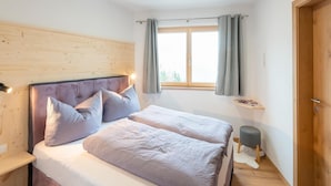 Ein Schlafzimmer mit einem hölzernen Kopfende, zwei Betten mit passender Bettwäsche, einem Nachttisch, einem Fenster mit Vorhängen und einer Tür.