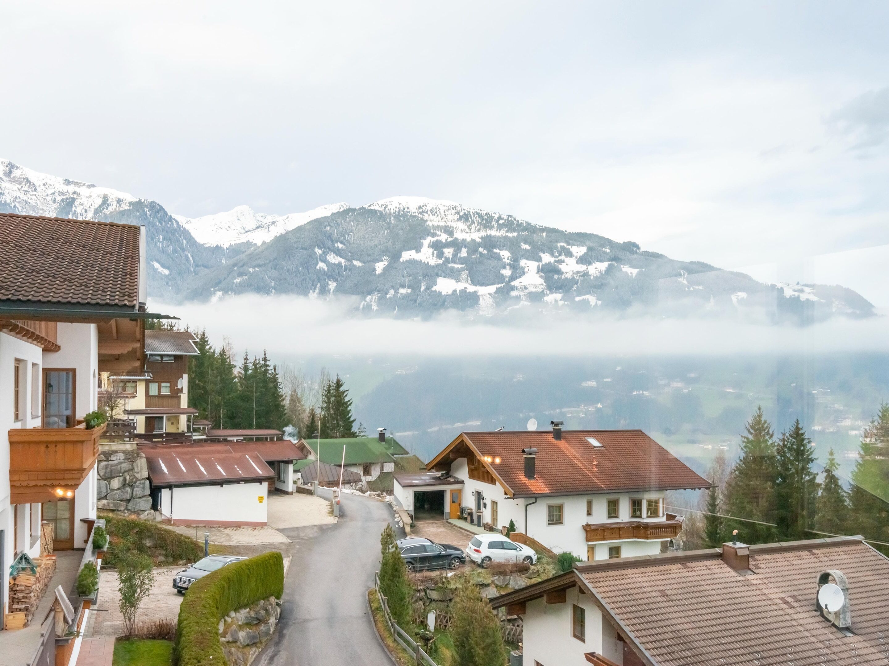 Un village de montagne à l’architecture traditionnelle, avec une route sinueuse et une vue sur des montagnes enneigées.