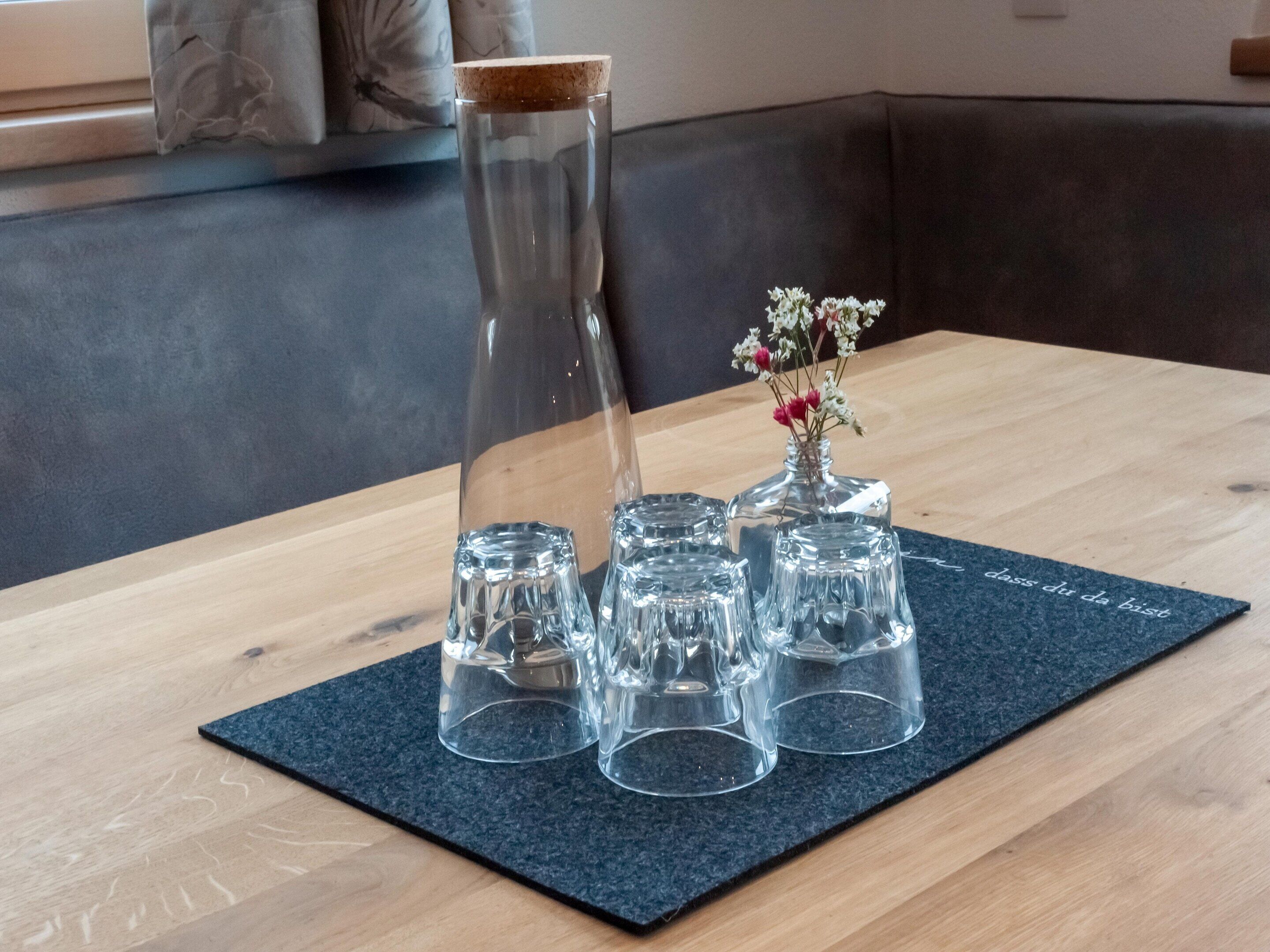 A table with a dark mat, a tall glass vase with a cork stopper, and three smaller glass vases with flowers.