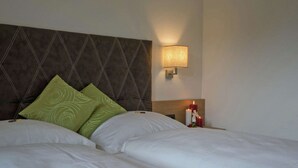 Ein Hotelzimmer mit einem großen Bett, zwei Kissen, einem Nachttisch mit Lampe und einer Wandleuchte.