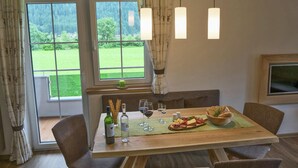 Ein Essbereich mit einem Holztisch, vier Stühlen, einer Kerze, Weingläsern und einer Käseplatte.