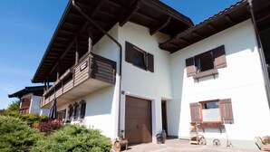 Ein zweistöckiges Gebäude mit Balkon, Garage und einer kleinen Außenbereich-Sitzgelegenheit mit Tisch und Stühlen.