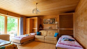 Ein gemütliches Blockhauss Zimmer mit Holzbalkendecke, einem Bett, einer Couch und einem Esstisch.