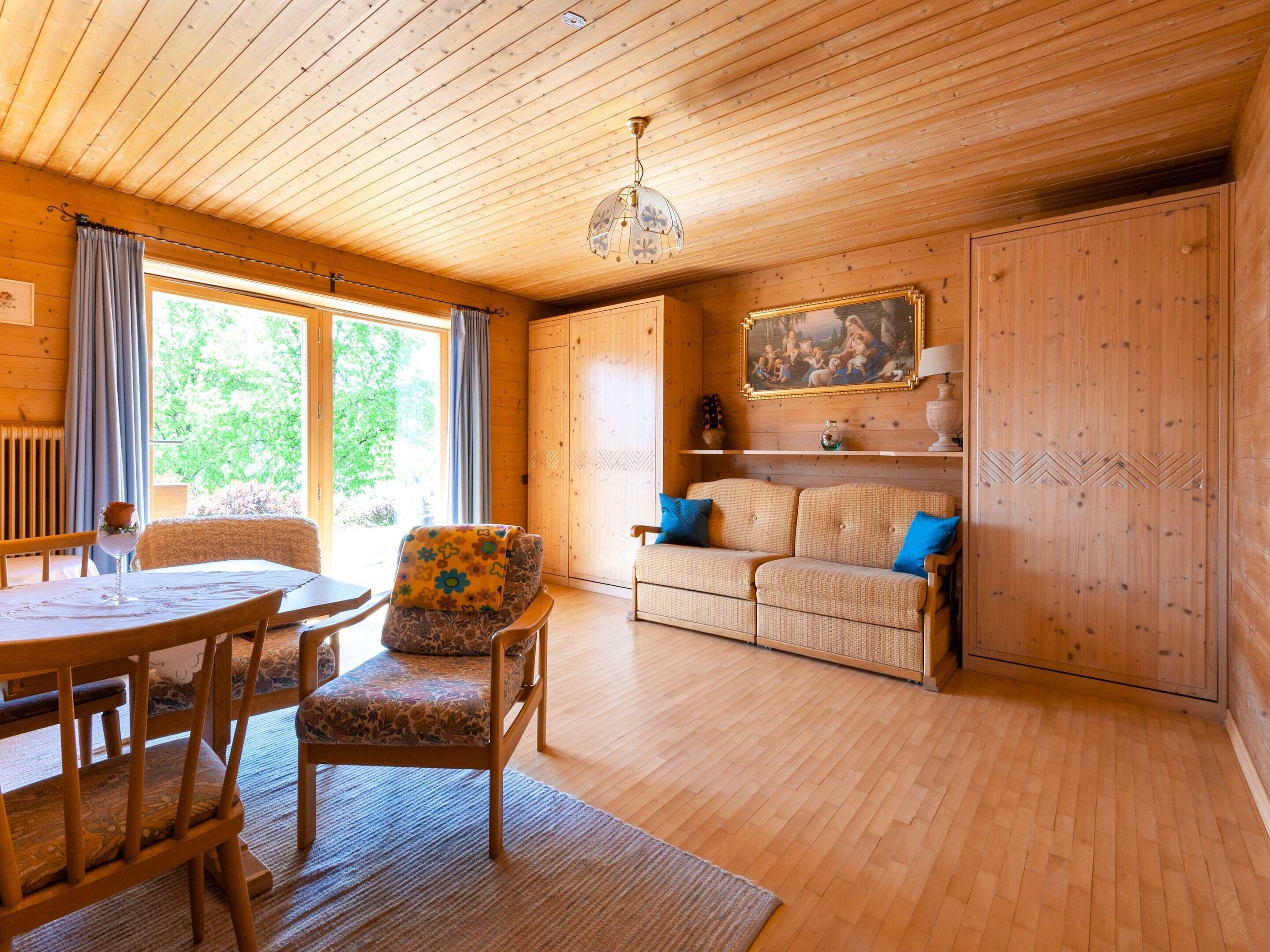 A wooden cabin interior with a dining area, sofa, and a painting on the wall.