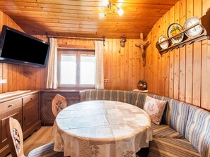 A wooden cabin interior with a round dining table, a sofa, a television, and wooden walls.