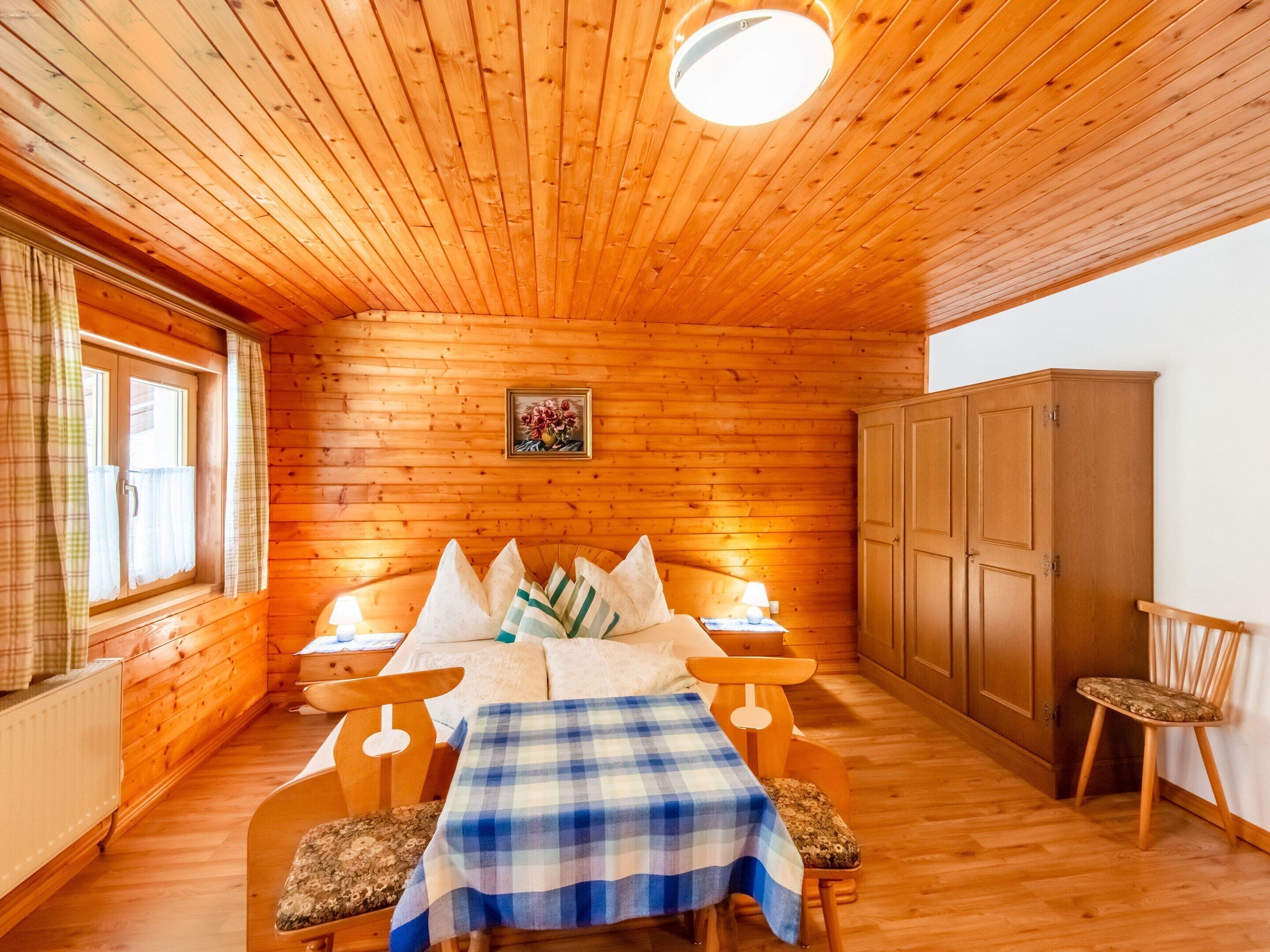 L’intérieur d’un chalet en bois comprend un lit, deux chaises, une table, une armoire et une fenêtre avec des rideaux.