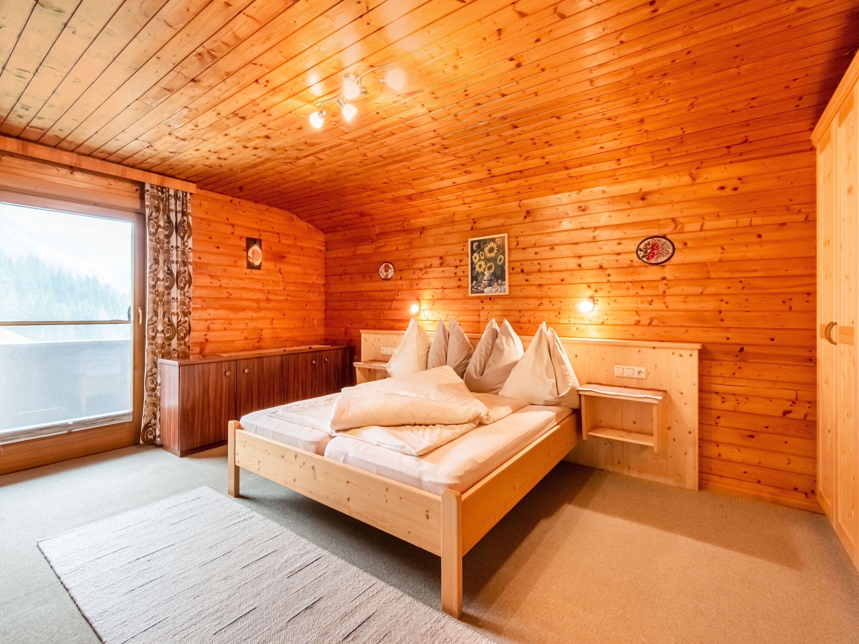 Un dormitorio de cabaña de madera con cama, mesitas de noche, ventana y puerta.