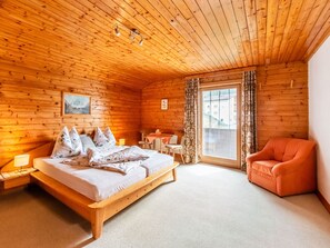 A wooden cabin bedroom with a bed, a chair, a table, and a window.