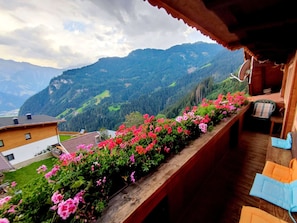 Un balcón con baranda de madera, con vistas a un paisaje montañoso con casas y vegetación.