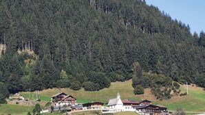 A cluster of buildings with a prominent white structure featuring a red roof, surrounded by lush greenery and a forested hillside. - Group Holiday Home in Hippach With Dreamy Views (Hippach)