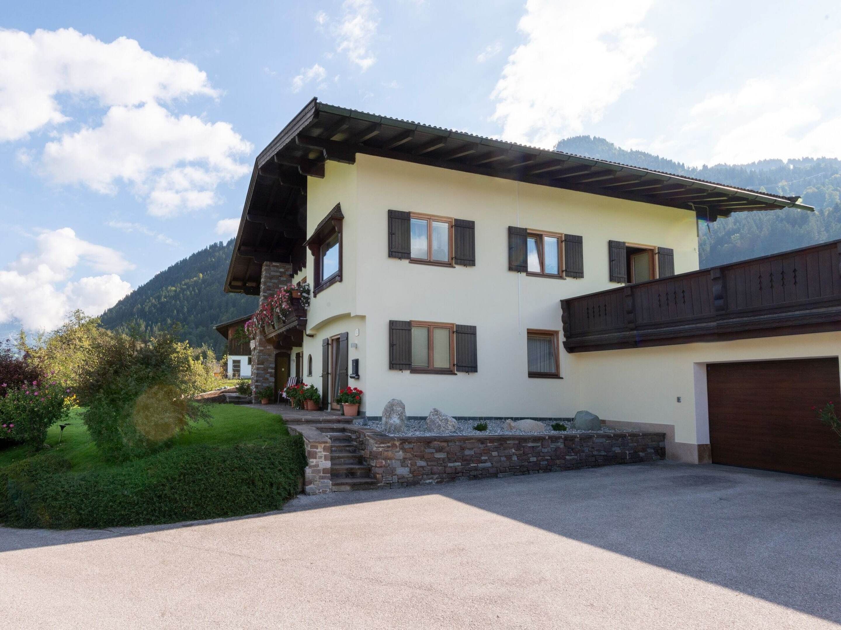 A two-story chalet with a stone facade, wooden shutters, and a balcony with potted plants.