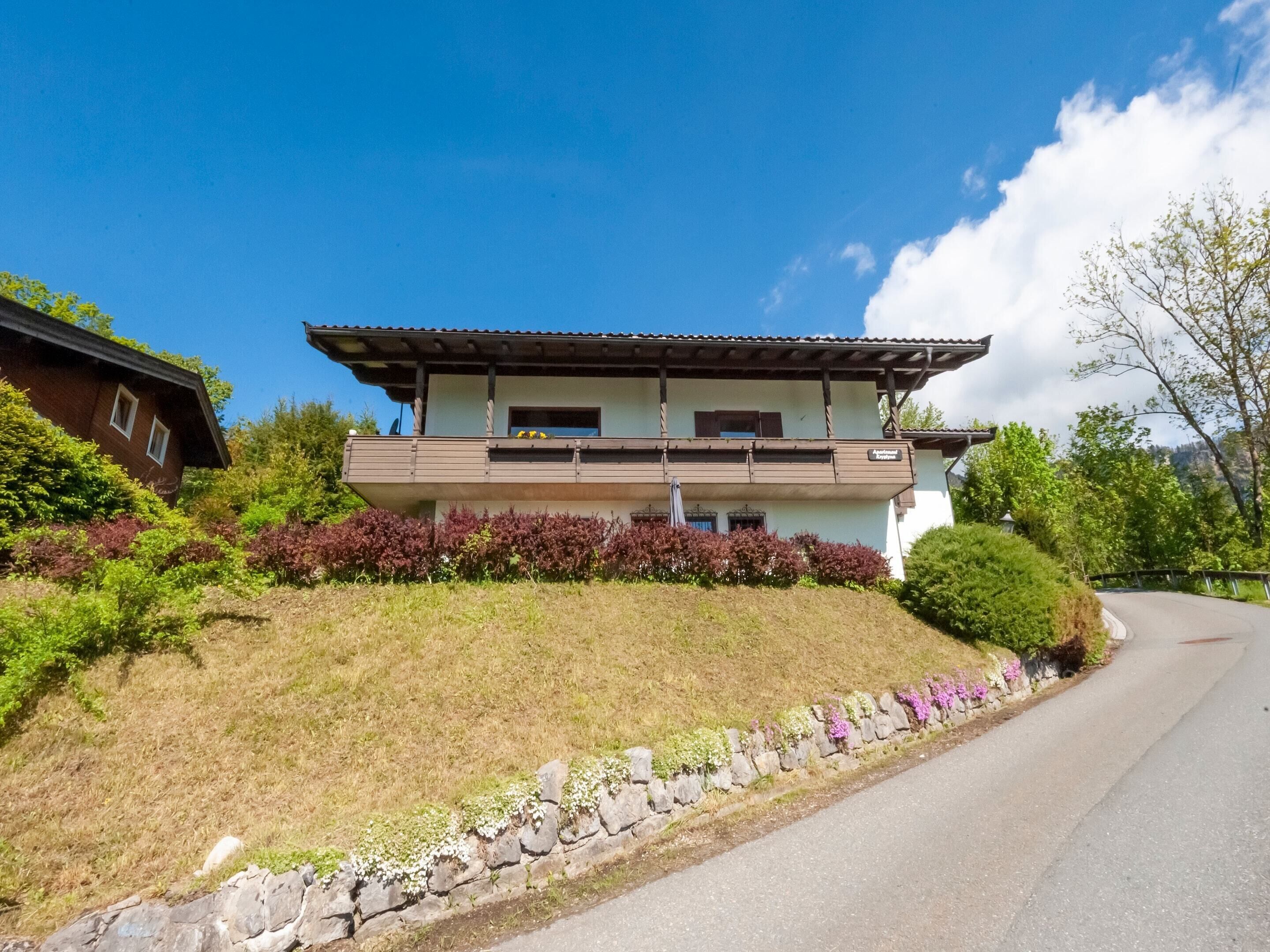 A two-story building with a balcony, surrounded by greenery and a stone wall.