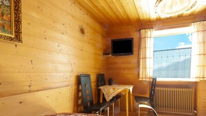 A cozy wooden cabin room with a bed, a table with chairs, a TV, and a window with curtains. - Apartment in St. Johann in Tyrol With Terrace (Sankt Johann in Tirol)