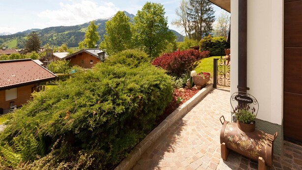 A stone pathway leading to a wooden door with a 'Willkommen' sign, surrounded by lush greenery and a mountain backdrop. - Apartment in St. Johann in Tyrol With Terrace (Sankt Johann in Tirol)