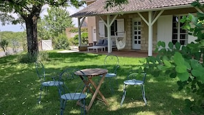 Un patio cubierto con mobiliario exterior, una hamaca y vistas de una casa con techo de tejas.
