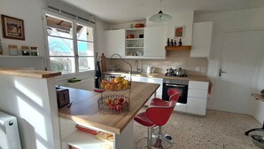 Una cocina moderna con armarios blancos, encimera de madera y un taburete rojo. Hay una cesta de frutas en la encimera y una ventana que proporciona luz natural.