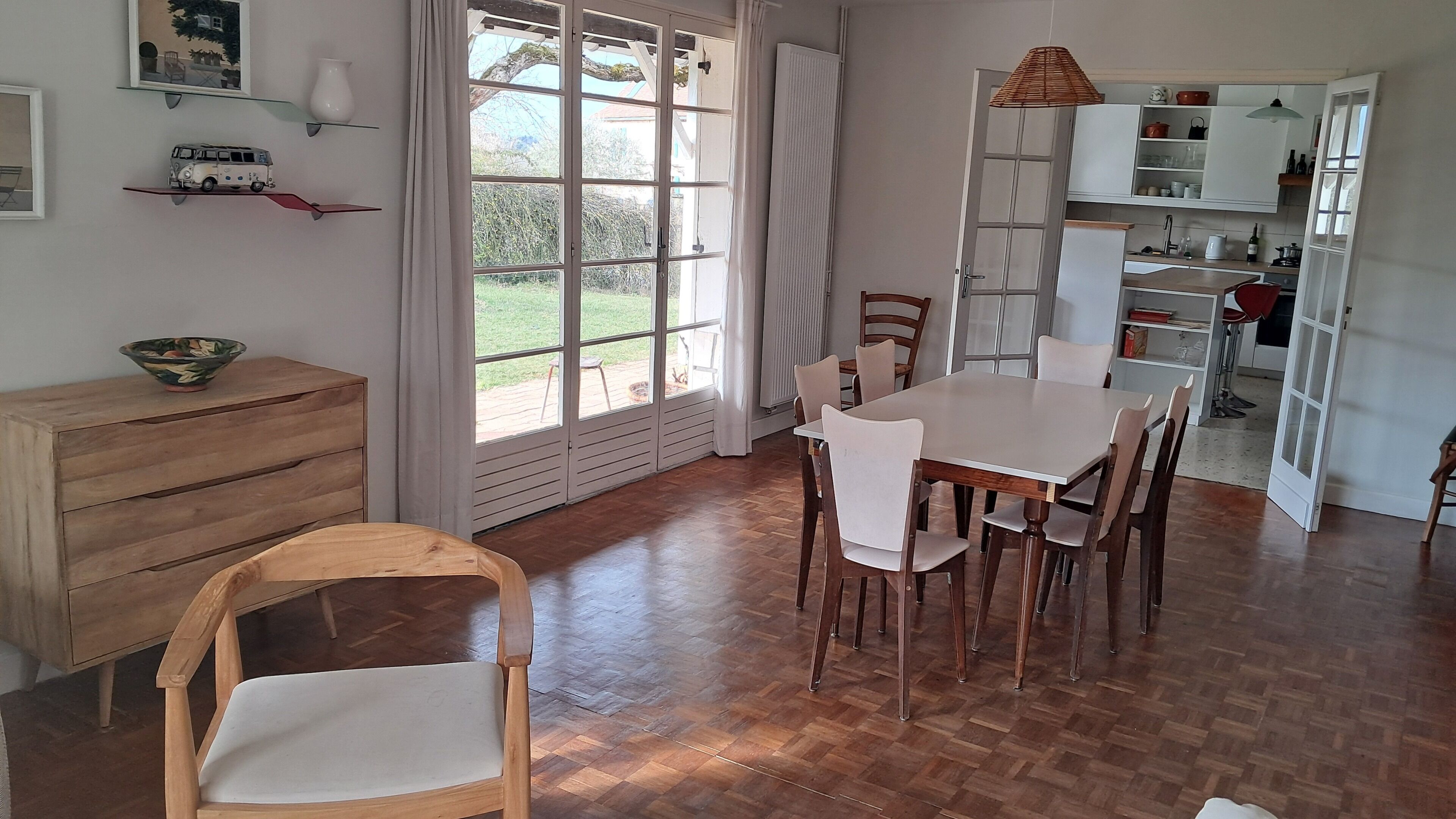 Ein Essbereich mit Holztisch und -stühlen, einem Holzschrank und einem großen Fenster mit Vorhängen.