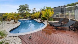 Una piscina con muelle de madera, sillones de descanso y plantas tropicales.