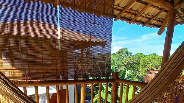 A hammock under a wooden roof with a view of greenery outside. - Casa Paula (Maraú)
