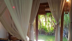 A bedroom with a bed, curtains, and a view of greenery outside. - Casa Paula (Maraú)