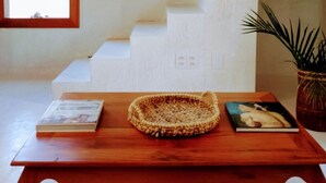 A staircase with white steps leading to a landing, a wooden table with a woven basket and books, and a window with blinds. - Casa Paula (Maraú)