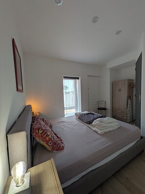 Un dormitorio con cama, mesitas de noche, una ventana y un armario.