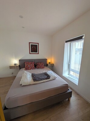 Une chambre à coucher avec un lit, une fenêtre, un tableau accroché au mur et des lampes de chevet.