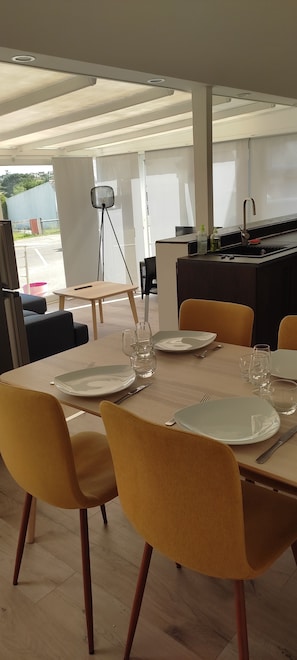 Un coin repas avec une table dressée pour quatre personnes, des chaises, une lampe sur pied et, au fond, un espace cuisine.