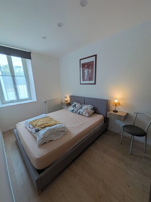 Une chambre à coucher avec un lit, des lampes de chevet, une chaise, une fenêtre et un tableau accroché au mur.