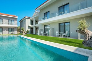 A modern hotel with a swimming pool, balconies with glass railings, and outdoor seating areas.